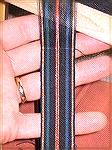 This little ribbon is being woven on an inkle loom.  The warp and weft are silk sewing thread, and the sparkly gold threads are a DMC metallic thread about the weight of buttonhole silk.

There are 